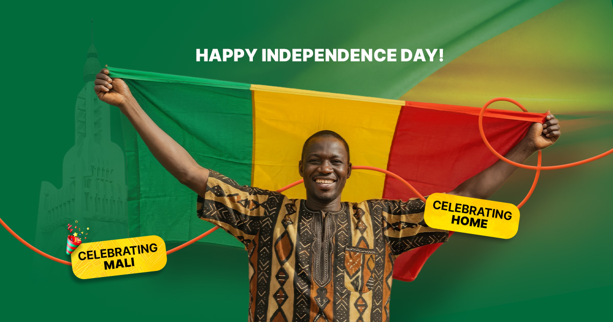 A smiling Malian man wearing a traditional patterned shirt holding the national flag of Mali to celebrate Mali’s Independence Day.