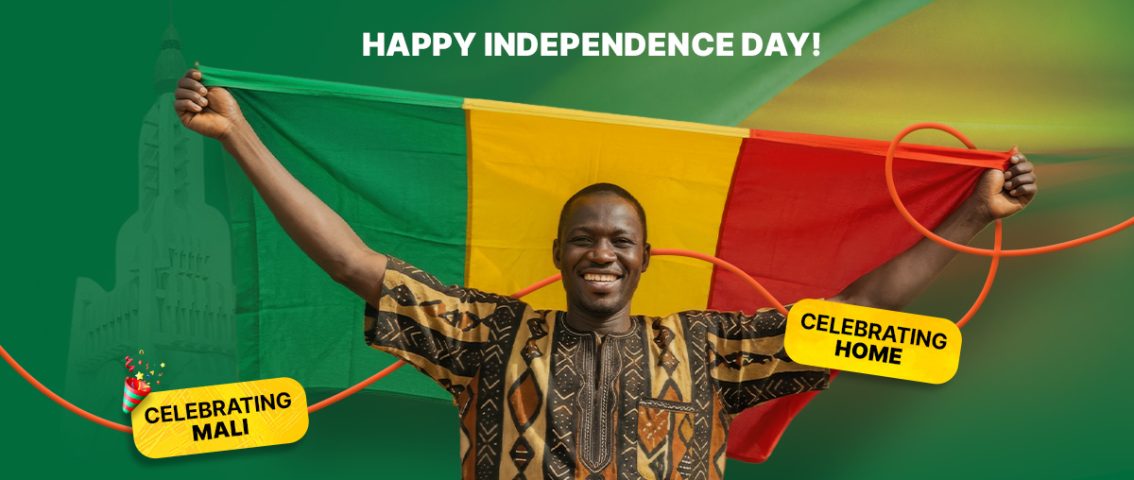 A smiling Malian man wearing a traditional patterned shirt holding the national flag of Mali to celebrate Mali’s Independence Day.