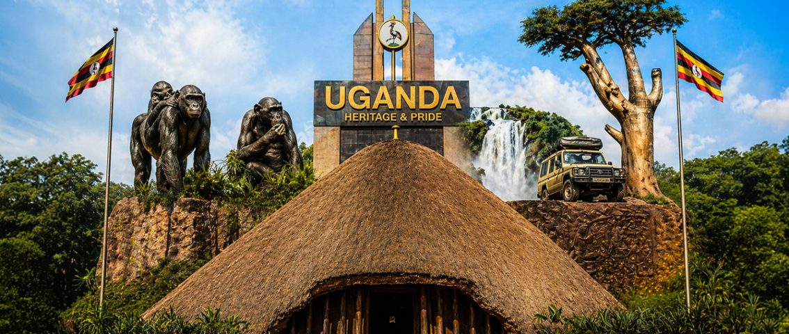 A digital collage celebrating Ugandan heritage under a blue sky, featuring a traditional thatched-roof building in the foreground, a monument reading "UGANDA HERITAGE & PRIDE," gorilla sculptures, a waterfall, a safari vehicle, a baobab tree, and two Ugandan flags.